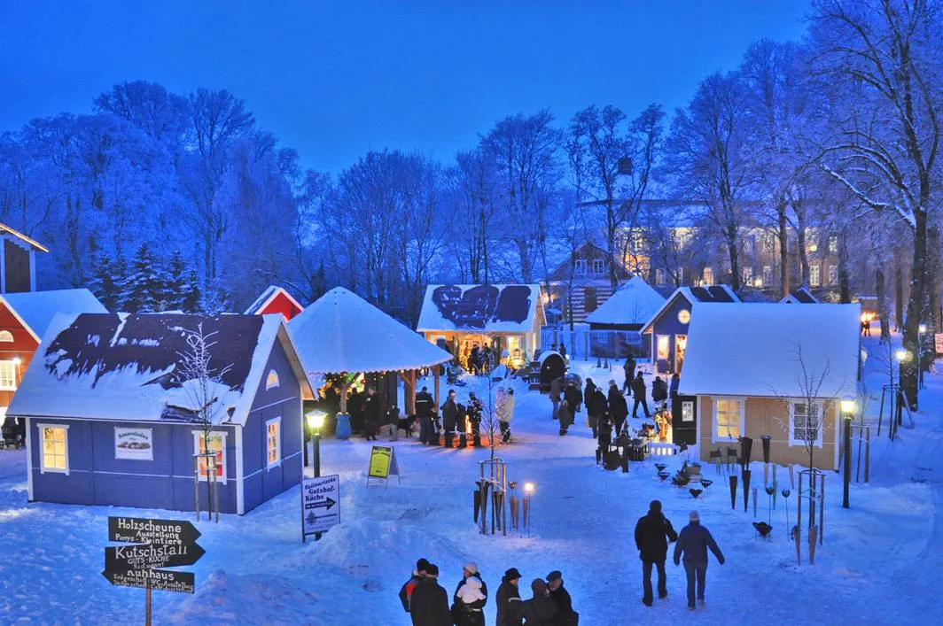 Verschneiter Pronstorfer Weihnachtsmarkt mit beleuchteten Holzhäusern in der blauen Stunde
